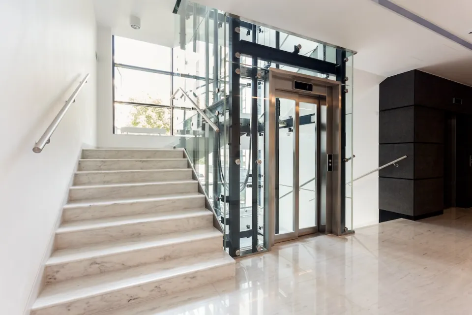 Concrete staircase next to elevator in bright building with large windows.